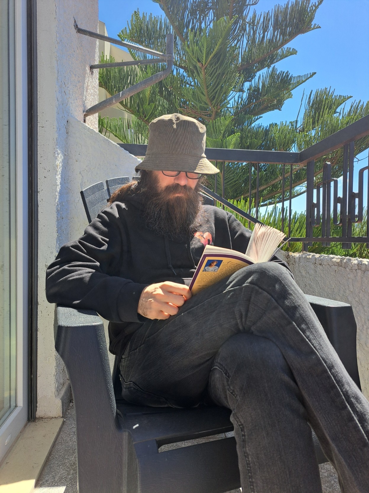 A guy (me) seated on a chair, reading a book (Rilla of Ingleside).